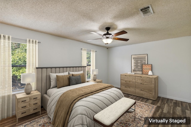 bedroom with a textured ceiling, ceiling fan, dark wood-type flooring, and multiple windows