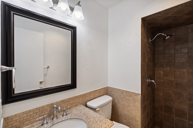 bathroom with a tile shower, sink, tile walls, and toilet