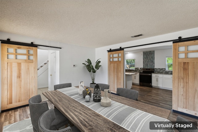 dining area featuring a barn door, dark hardwood / wood-style flooring, and a textured ceiling