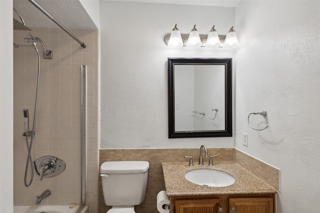 full bathroom with vanity, toilet, tiled shower / bath, and tile walls