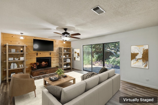 living room featuring ceiling fan, wood walls, wood-type flooring, a textured ceiling, and a fireplace