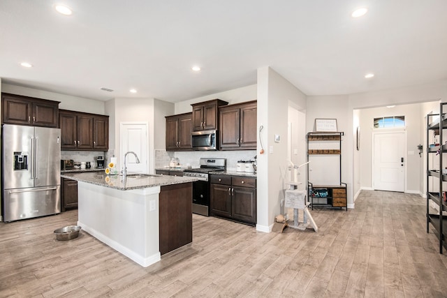 kitchen with appliances with stainless steel finishes, sink, light stone counters, light hardwood / wood-style flooring, and a center island with sink