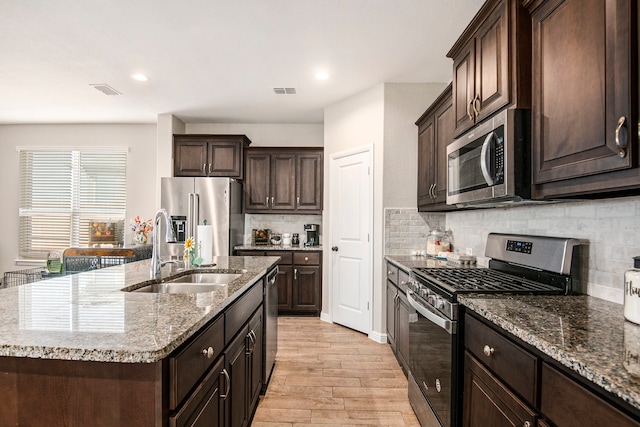 kitchen with decorative backsplash, appliances with stainless steel finishes, a kitchen island with sink, light hardwood / wood-style flooring, and sink