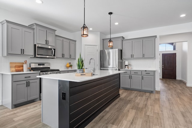 kitchen featuring light hardwood / wood-style floors, stainless steel appliances, a center island with sink, and gray cabinets