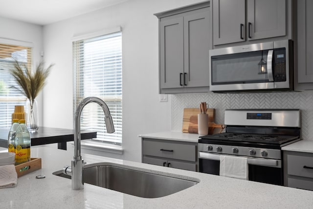 kitchen with tasteful backsplash, appliances with stainless steel finishes, sink, gray cabinets, and light stone counters