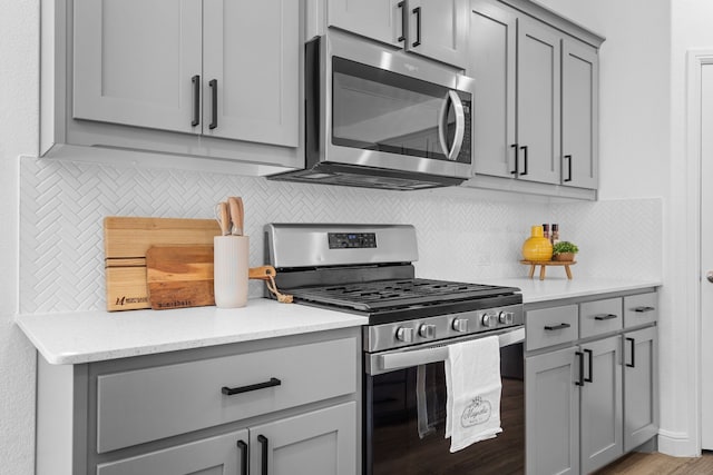 kitchen with light stone counters, tasteful backsplash, appliances with stainless steel finishes, and light hardwood / wood-style flooring