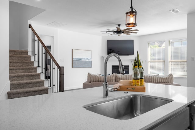 kitchen featuring ceiling fan, light stone countertops, sink, and hanging light fixtures