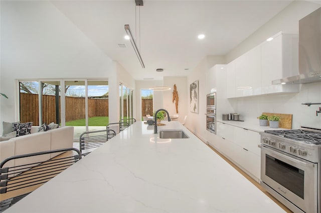 kitchen featuring wall chimney range hood, tasteful backsplash, high end stove, white cabinetry, and pendant lighting