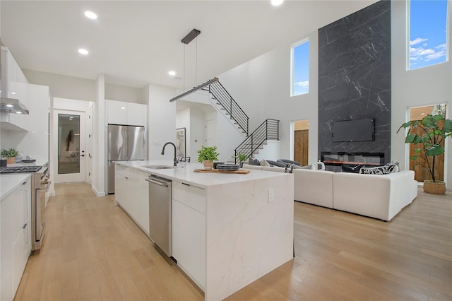 kitchen featuring a center island with sink, sink, white cabinets, pendant lighting, and appliances with stainless steel finishes