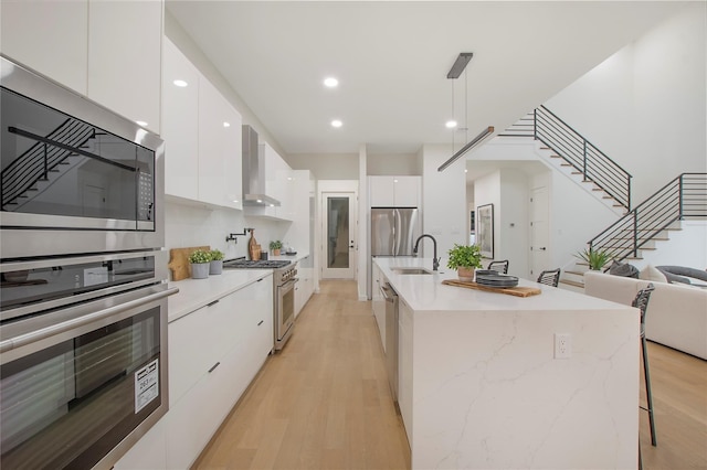 kitchen featuring stainless steel appliances, sink, decorative light fixtures, light wood-type flooring, and white cabinets