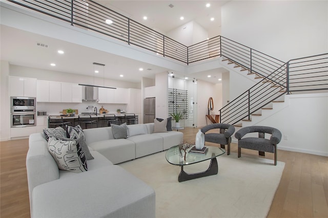 living room with sink, a high ceiling, and light hardwood / wood-style flooring