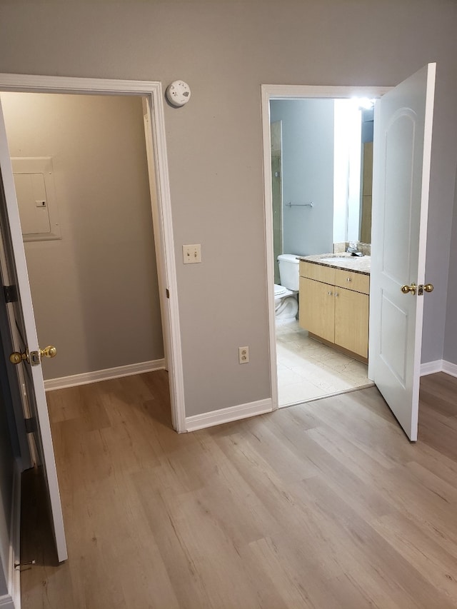 unfurnished bedroom with connected bathroom, sink, electric panel, and light wood-type flooring