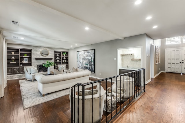 living room featuring sink, dark wood-type flooring, built in features, and a brick fireplace