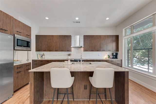 kitchen featuring wall chimney exhaust hood, appliances with stainless steel finishes, a healthy amount of sunlight, and an island with sink