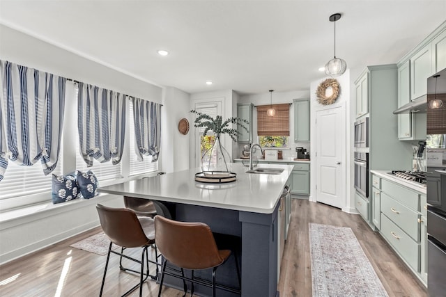 kitchen with a center island with sink, stainless steel appliances, decorative light fixtures, and sink