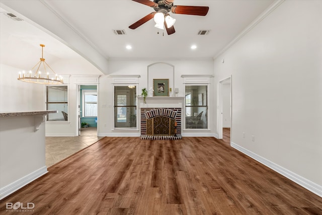 unfurnished living room with ornamental molding, hardwood / wood-style floors, a brick fireplace, and ceiling fan with notable chandelier