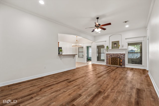 unfurnished living room with ornamental molding, a fireplace, wood-type flooring, and ceiling fan with notable chandelier