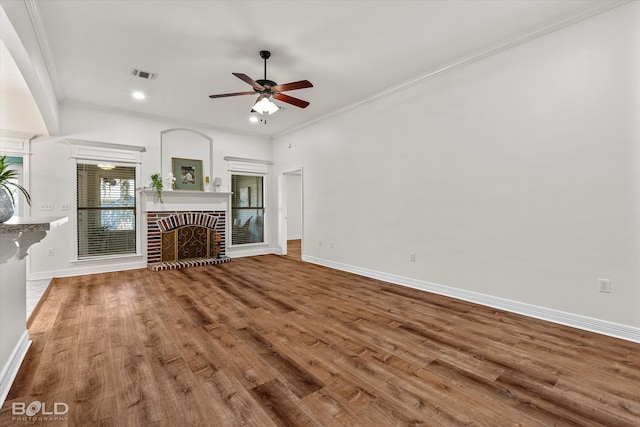 unfurnished living room featuring ceiling fan, wood-type flooring, ornamental molding, and a fireplace