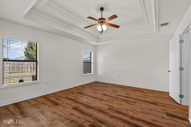 empty room with crown molding, a healthy amount of sunlight, wood-type flooring, and a tray ceiling