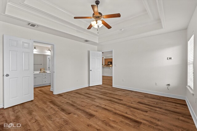 unfurnished bedroom with a raised ceiling, ceiling fan, wood-type flooring, crown molding, and ensuite bath