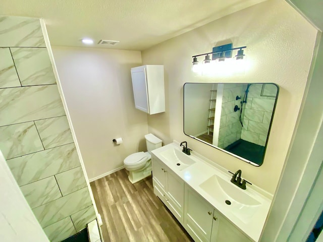 bathroom featuring vanity, tiled shower, wood-type flooring, and toilet