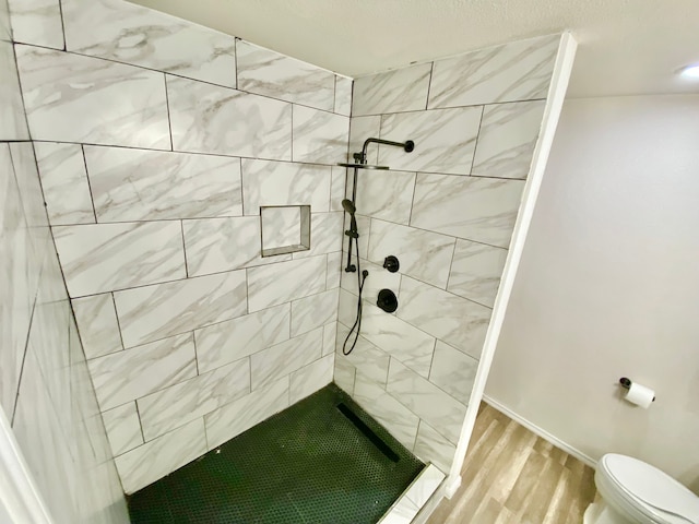 bathroom with a tile shower, hardwood / wood-style flooring, and toilet