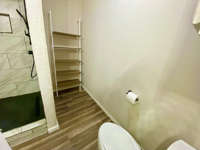 bathroom featuring a tile shower, wood-type flooring, and toilet