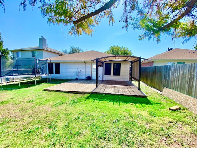 rear view of property featuring a deck, a yard, and a trampoline