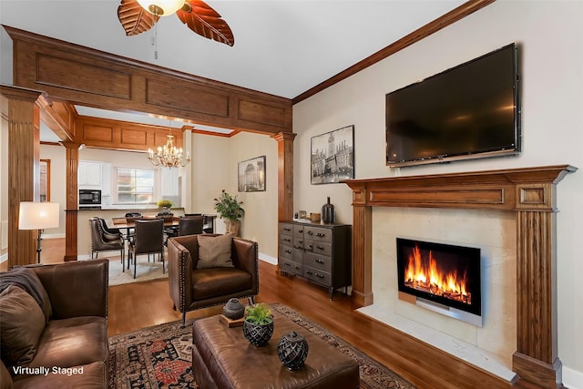 living room with a premium fireplace, crown molding, dark wood-type flooring, and ceiling fan with notable chandelier