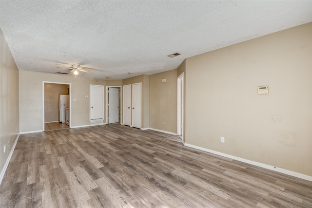 unfurnished room with a textured ceiling, light wood-type flooring, and ceiling fan