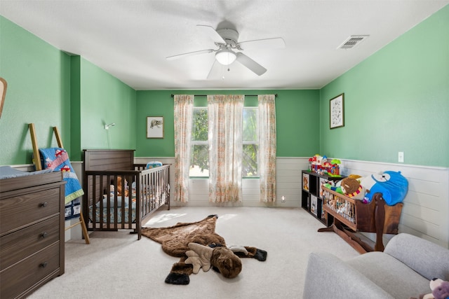 bedroom with ceiling fan, a crib, and light carpet