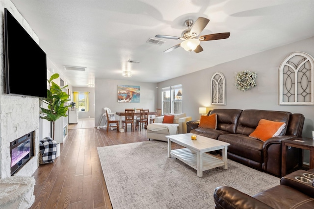 living room featuring a stone fireplace, ceiling fan, and wood-type flooring