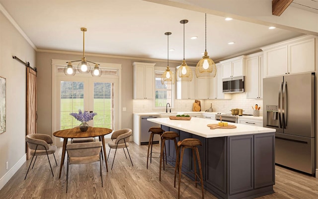 kitchen with a center island with sink, hanging light fixtures, appliances with stainless steel finishes, white cabinetry, and a barn door