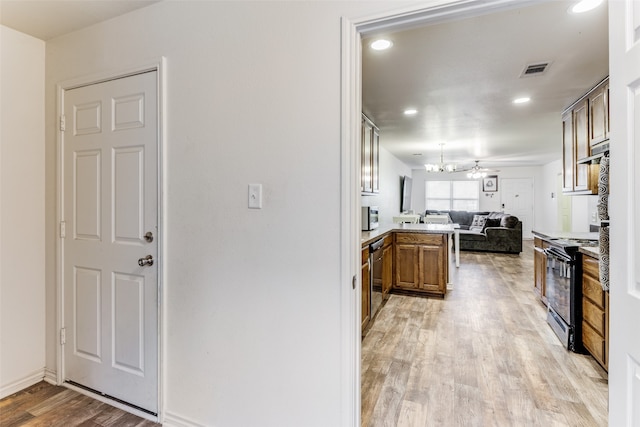 kitchen with light hardwood / wood-style flooring, kitchen peninsula, a notable chandelier, and black range oven