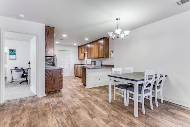 kitchen with kitchen peninsula, sink, a notable chandelier, pendant lighting, and light hardwood / wood-style floors