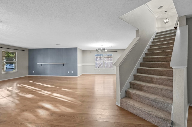 stairway featuring a textured ceiling, wood-type flooring, an inviting chandelier, and plenty of natural light