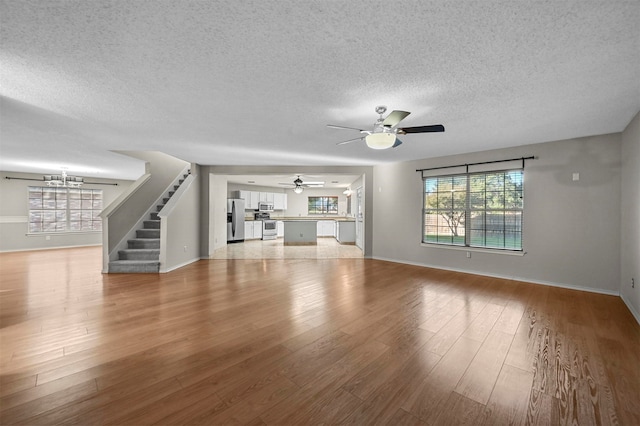 unfurnished living room with ceiling fan with notable chandelier, a textured ceiling, and light hardwood / wood-style floors