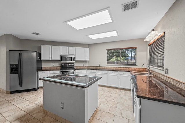 kitchen featuring white cabinetry, dark stone countertops, stainless steel appliances, sink, and a center island