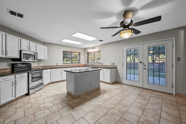 kitchen with appliances with stainless steel finishes, a kitchen island, french doors, white cabinetry, and ceiling fan