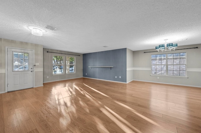 unfurnished living room with hardwood / wood-style floors, a textured ceiling, and an inviting chandelier