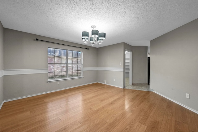 empty room with a chandelier, a textured ceiling, and light hardwood / wood-style floors