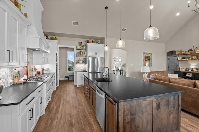 kitchen with appliances with stainless steel finishes, sink, pendant lighting, white cabinets, and a center island with sink