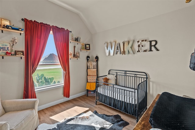 bedroom featuring a crib, light wood-type flooring, and vaulted ceiling