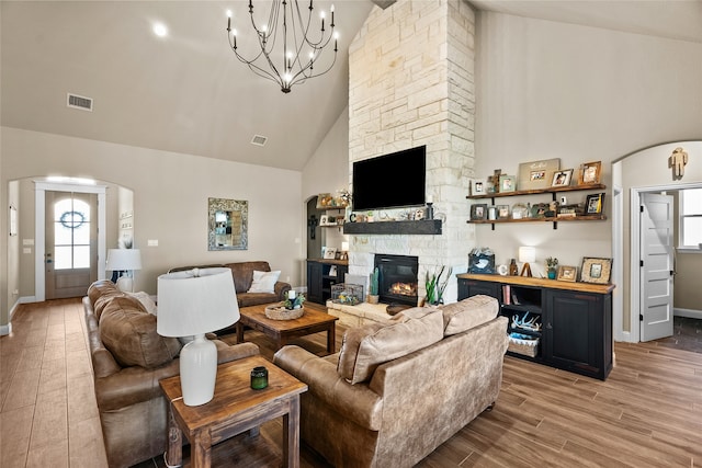 living room with a stone fireplace, hardwood / wood-style flooring, high vaulted ceiling, and a chandelier