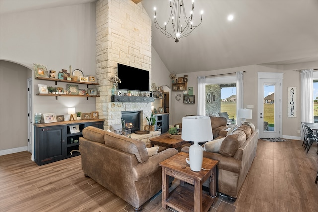 living room featuring high vaulted ceiling, a stone fireplace, light hardwood / wood-style flooring, and a chandelier