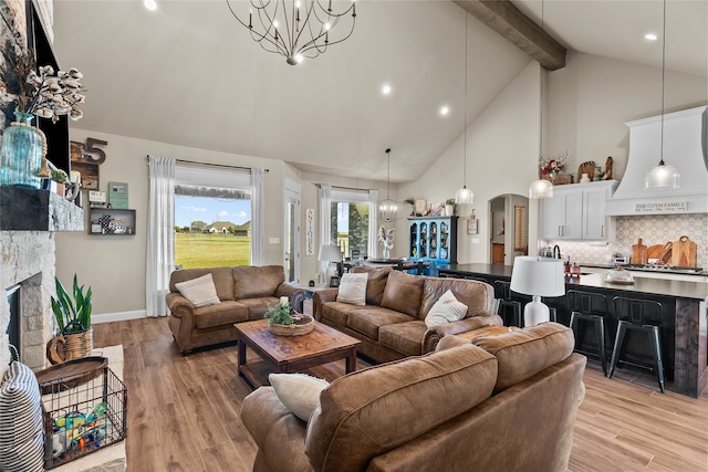 living room with beamed ceiling, light hardwood / wood-style flooring, a notable chandelier, a fireplace, and high vaulted ceiling