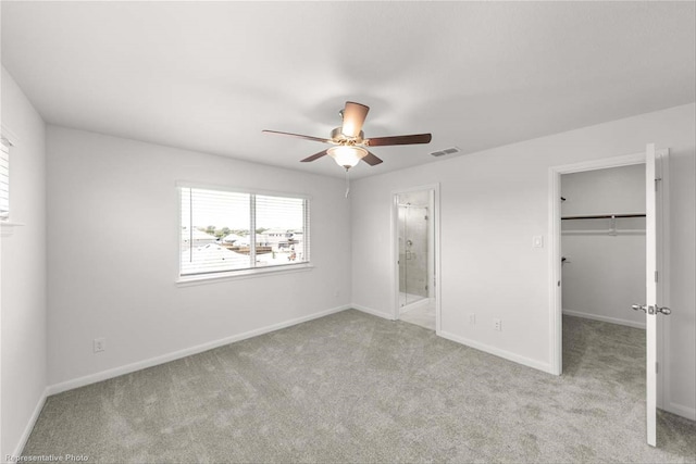 unfurnished bedroom with a closet, a walk in closet, ensuite bath, light colored carpet, and ceiling fan