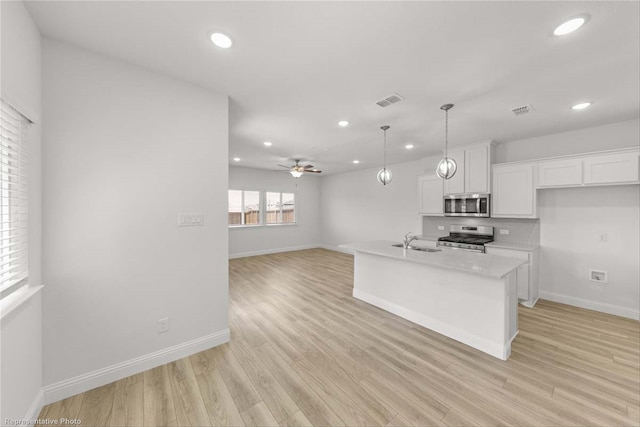 kitchen with white cabinetry, appliances with stainless steel finishes, an island with sink, and light hardwood / wood-style flooring