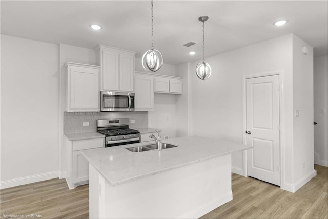 kitchen with light wood-type flooring, appliances with stainless steel finishes, sink, white cabinets, and a kitchen island with sink