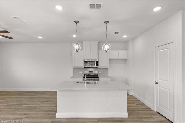 kitchen featuring stainless steel appliances, light hardwood / wood-style floors, white cabinets, an island with sink, and backsplash